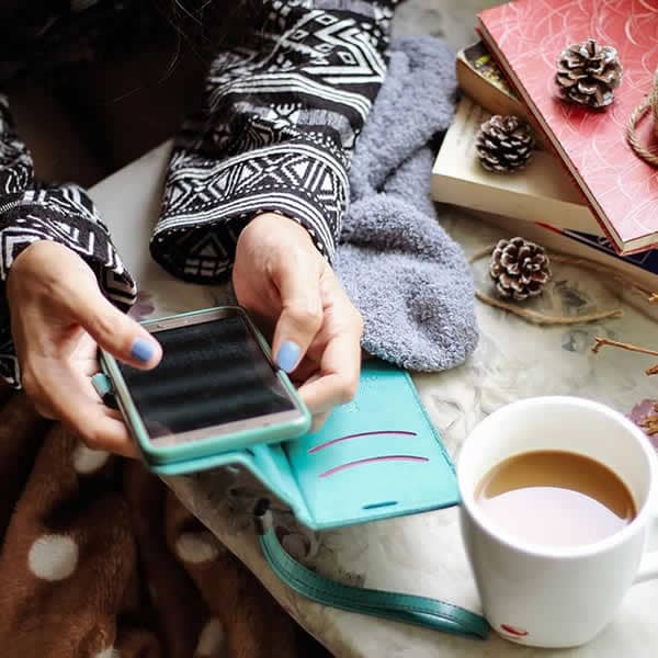 Persona revisando su teléfono móvil para comunicarse, junto a una taza de café, representando un momento de contacto y atención personalizada.